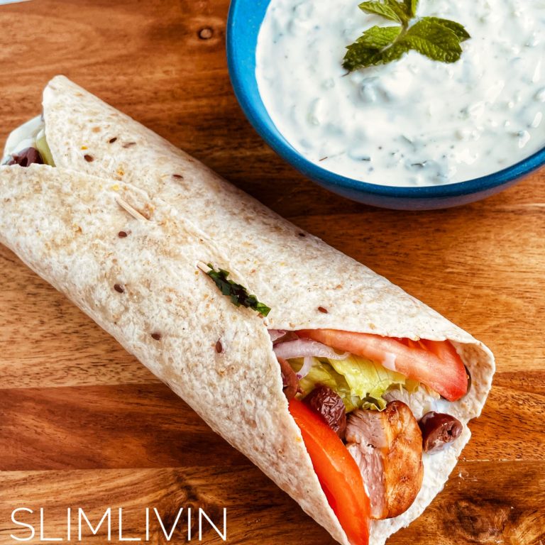 Greek chicken wrap on a board next a bowl of tzatziki